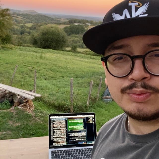 Portrait of Toz, smiling, with a laptop and green hills behind
